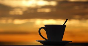 A cup of Kona coffee with a sunset view by the shore