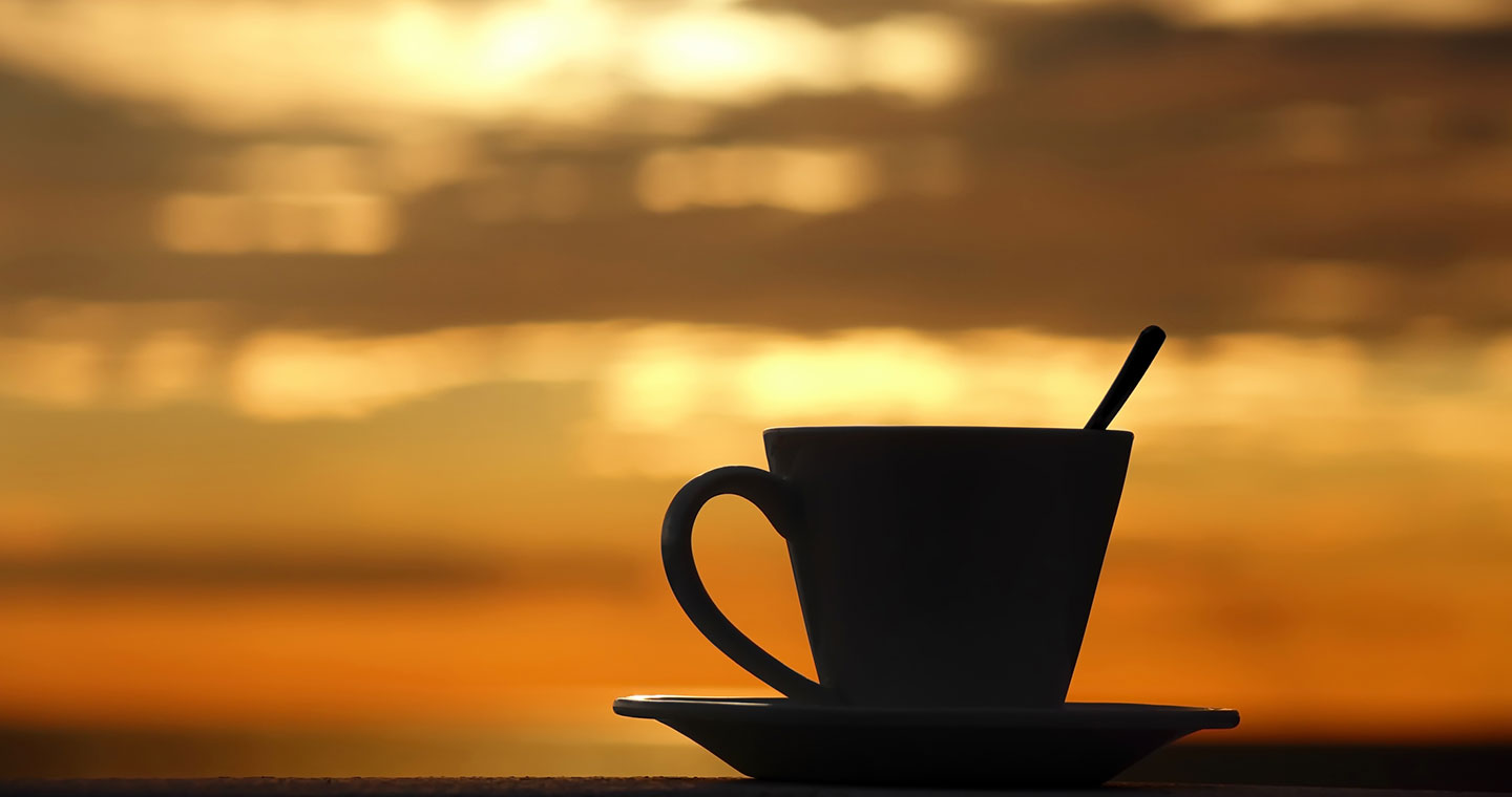 A cup of Kona coffee with a sunset view by the shore