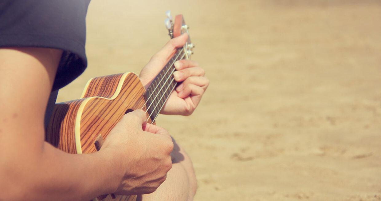 A person playing the ukulele while sitting on the sand