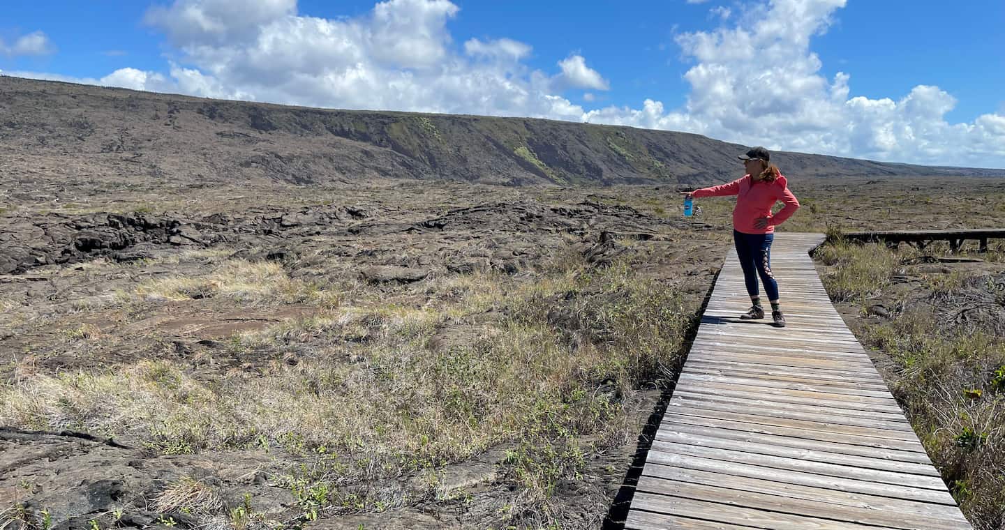 A woman walks along a wooden boardwalk through a rugged lava field, at Hawaii Volcanoes National Park.