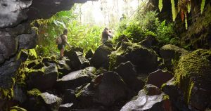 Two women hiking over large rocks in the Kaumana Caves on the Big Island