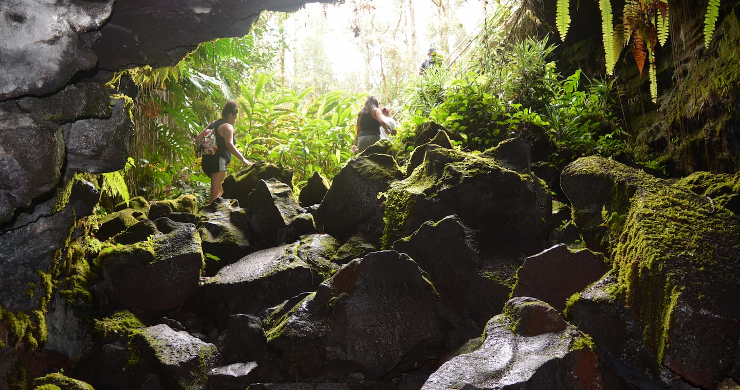 Two women hiking over large rocks in the Kaumana Caves on the Big Island