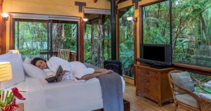 A woman curled up in bed reading a in a private lodge at our Big Island bed and breakfast