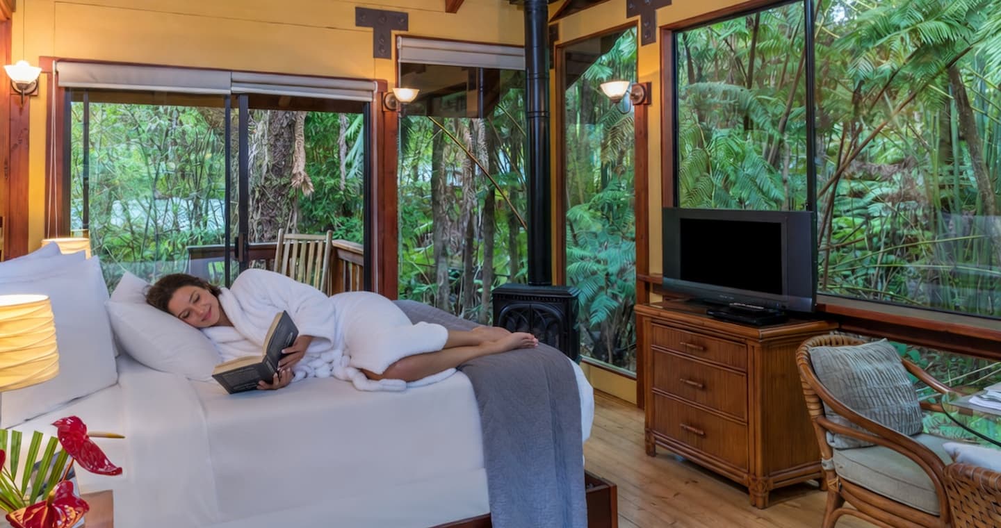 A woman curled up in bed reading a in a private lodge at our Big Island bed and breakfast