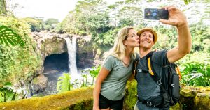 A couple taking a selfie in front of Rainbow Falls in Hilo during a last minute Hawaii vacation