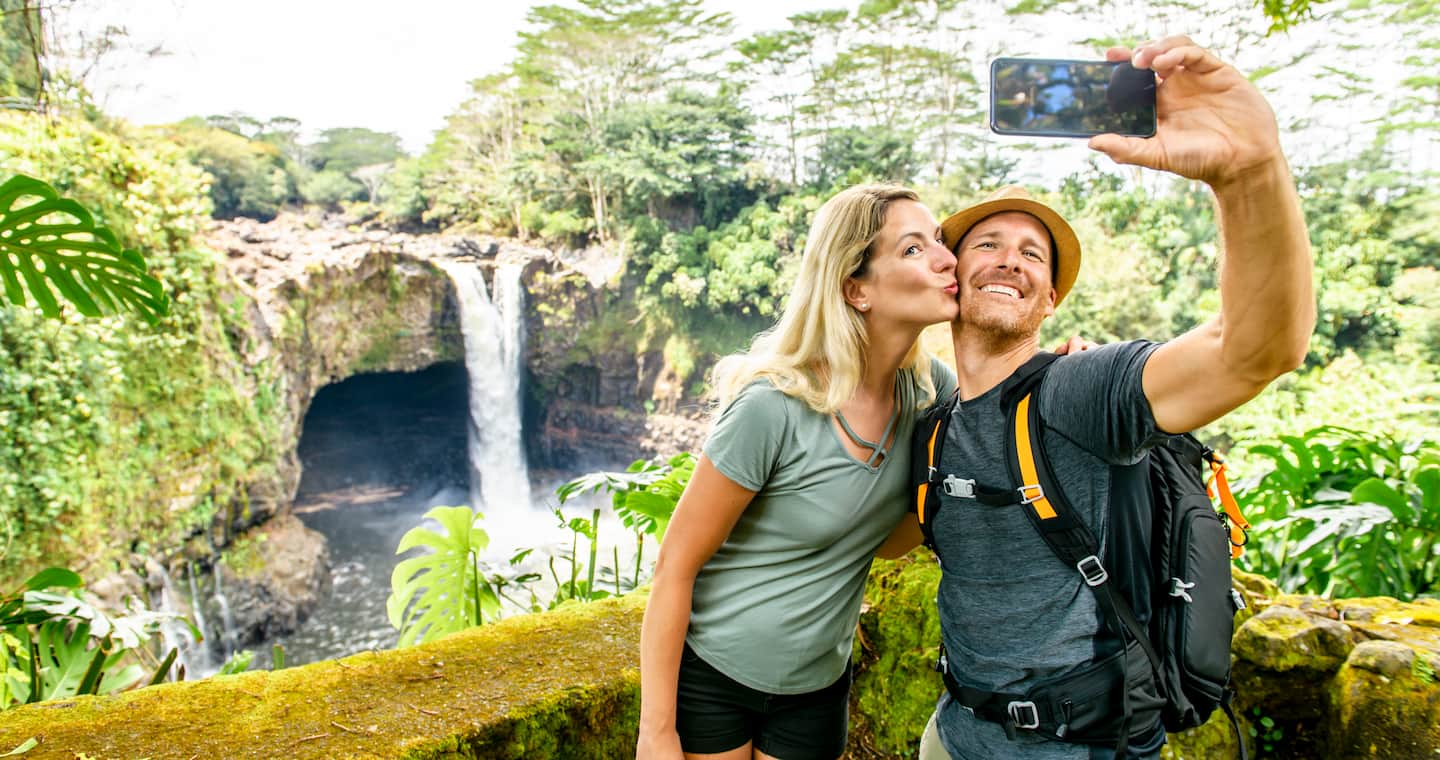 A couple taking a selfie in front of Rainbow Falls in Hilo during a last minute Hawaii vacation